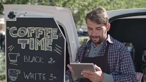 Coffee-Truck-Worker-Leaning-On-The-Van-While-Using-A-Tablet