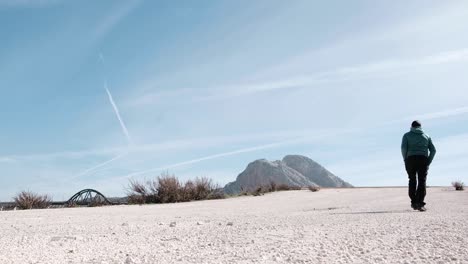 Person-walks-in-a-mountainous-landscape-with-clear-blue-sky-background