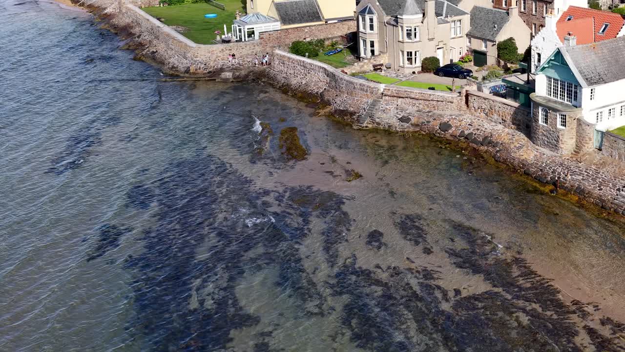 Drone glider over kystby og afslører historiske huse, stendæmning og naturskøn kystlinje