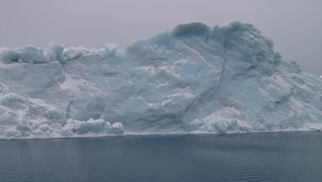 Iceberg-Azul-Aguamarina-Flota-En-El-Océano-Bajo-Un-Cielo-Nublado-Frente-A-La-Costa-De-Groenlandia