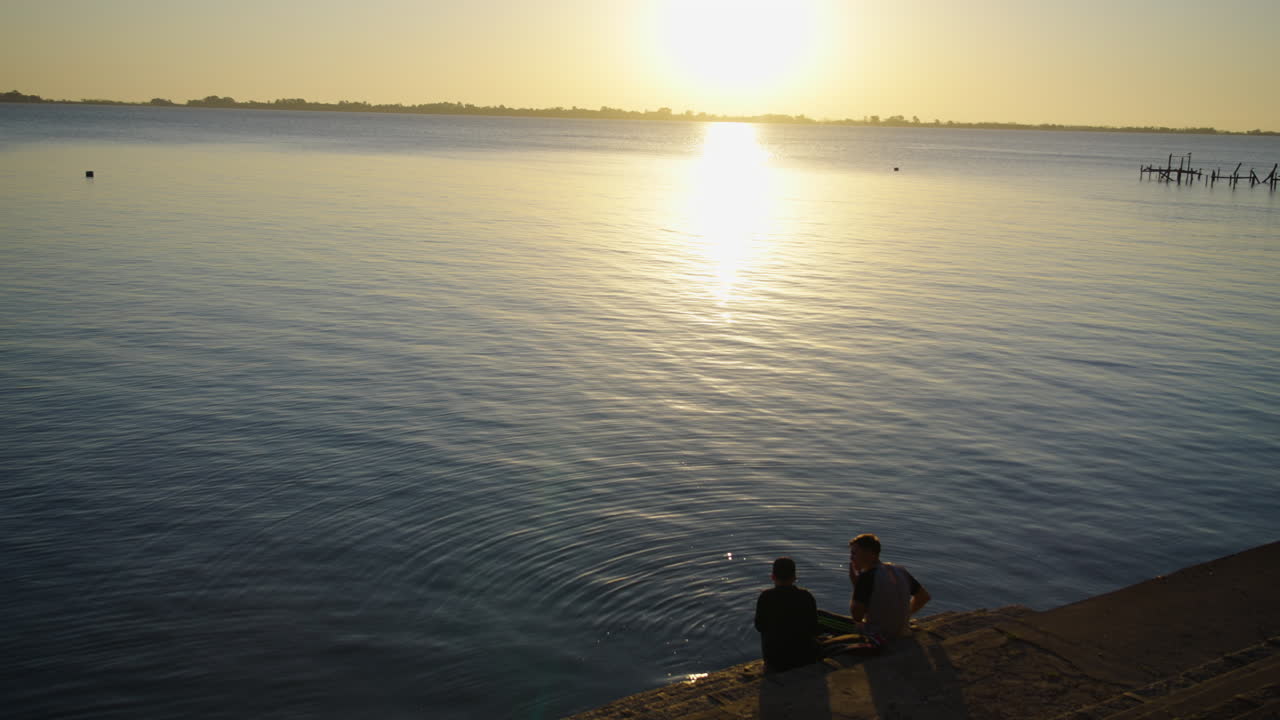 Due persone sedute vicino all'acqua calma del lago all'ora d'oro
