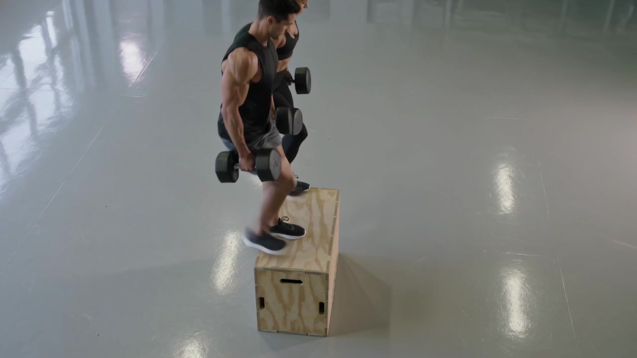 Starting rep, duo in black doing weighted step-ups in studio with dumbbells, plyo box for strength