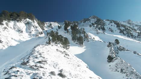 Vista-Aérea-De-Drones-Volando-Alrededor-De-Una-Hermosa-Montaña-Cubierta-De-Nieve-Y-árboles-Con-Un-Cielo-Azul-Profundo