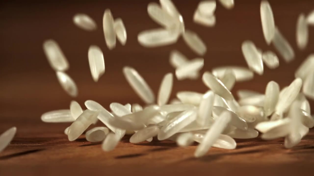 Chicchi di riso bianco che cadono al rallentatore su una superficie di legno