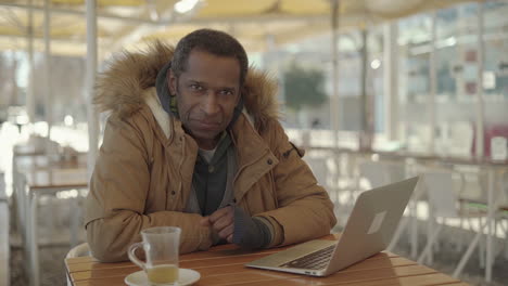 man typing on laptop and smiling at camera in cafe