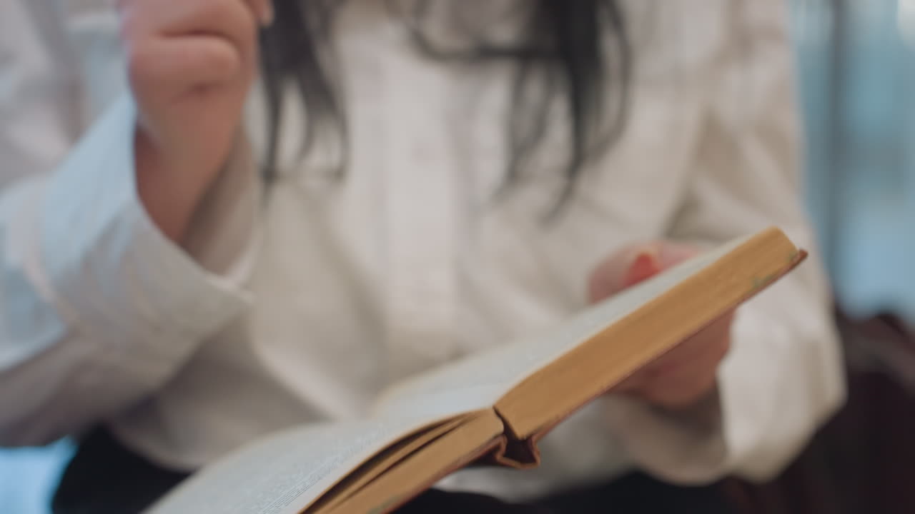 Close up of fair skin lady holding open book in both hands gently moving while dancing, focus on old pages with blurred white shirt and dark hair in background