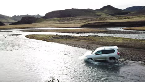 four wheel vehicle crossing glacial river in valley of iceland highlands, aerial view