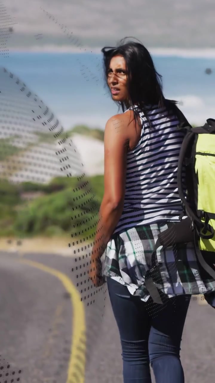 Video vertical: Mujer caminando por una carretera costera, buscando información de viaje con el pulgar, con una superposición punteada de neón.