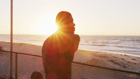 Hombre-Afroamericano-Enfocado-Estirándose,-Haciendo-Ejercicio-Al-Aire-Libre-Junto-Al-Mar-Al-Atardecer