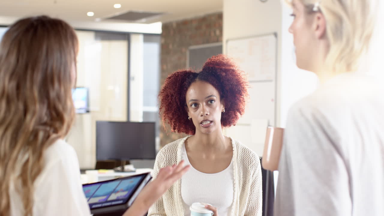 Discutindo ideias, mulheres colaborando no escritório, uma tomando café, outras conversando