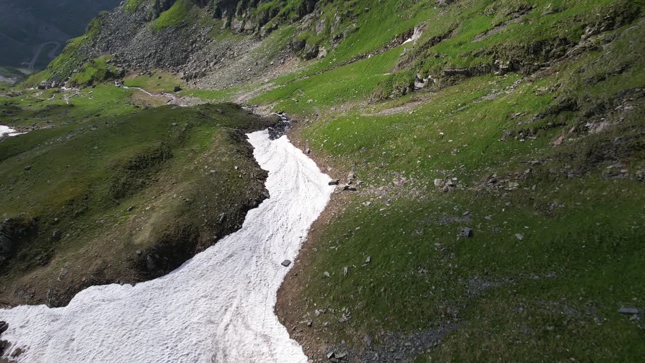cinematográfico fpv drone aéreo 4k video sobre el valle de la montaña con nieve, río, rocas y hierba verde en primavera