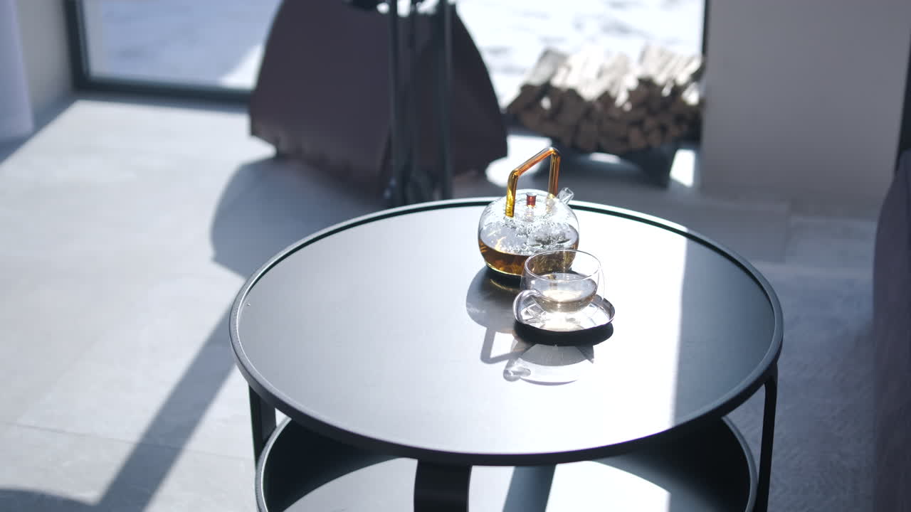 Tetera y taza de cristal sobre mesa de centro moderna con luz solar