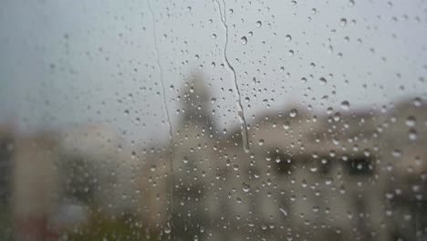 view of raindrops landing on a window glass during heavy rainfall, , with an urban city landscape in the background