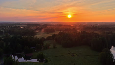 aerial of vibrant orange sunrise sunset over misty landscape and treetops in the distance