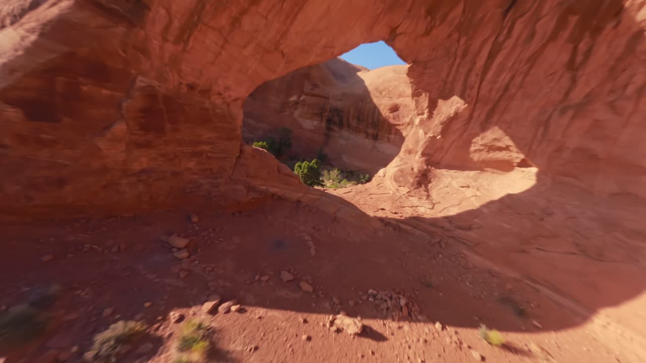 An FPV flying towards and through the hidden red sandstone Funnel Arch in the sandy and rocky desert of Moab Utah