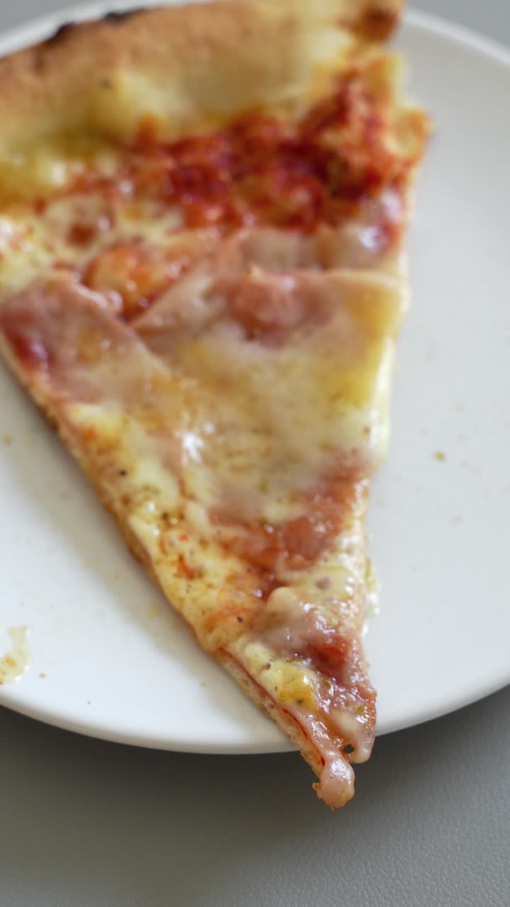 Fresh, greasy slice of Italian pizza with bubbling cheese on a white plate