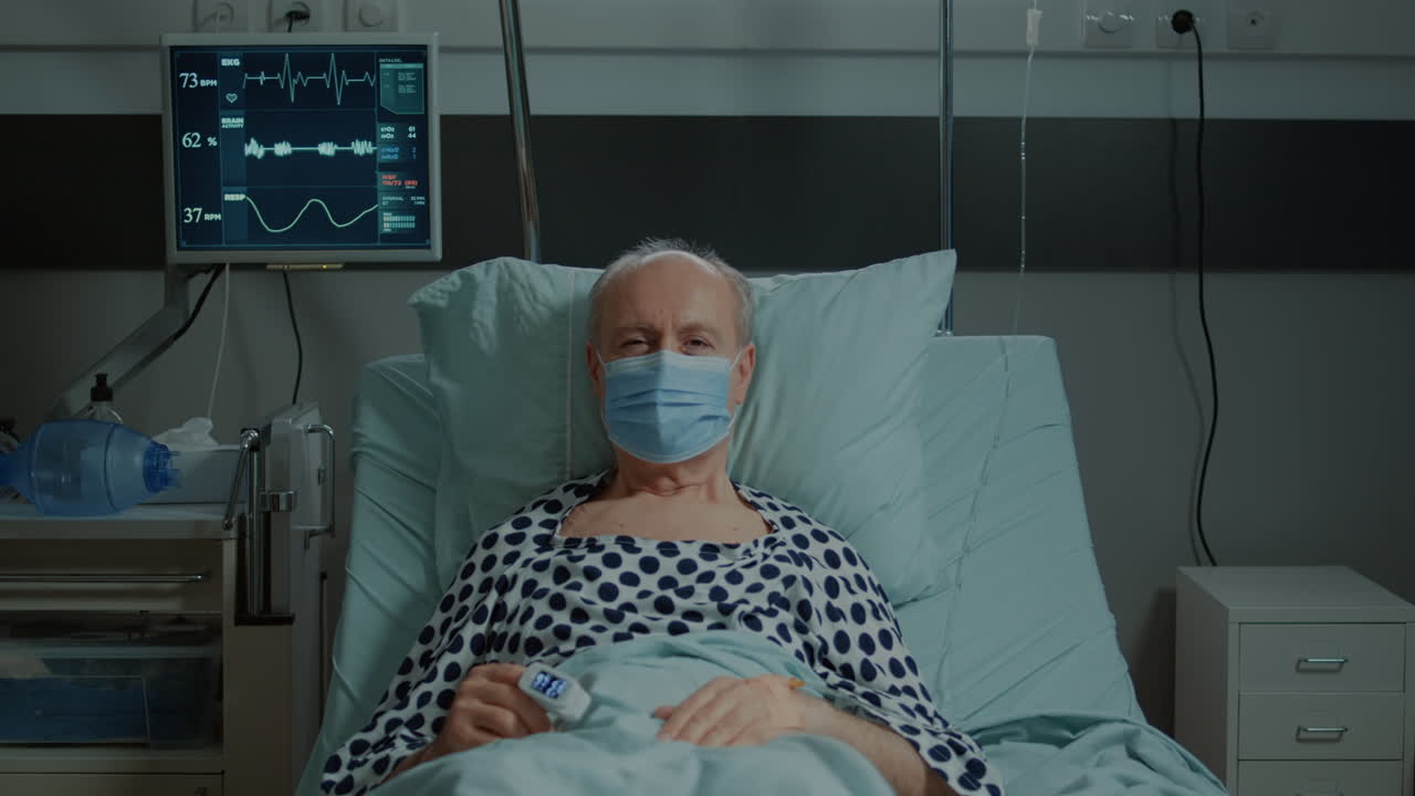 Portrait of old patient with face mask sitting in hospital ward