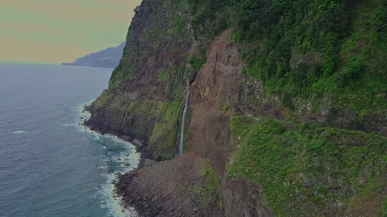 antena en órbita de una serena cascada que desemboca en el océano desde las montañas, madeira