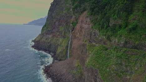 orbiting aerial of serene waterfall flowing into ocean from mountains, madeira