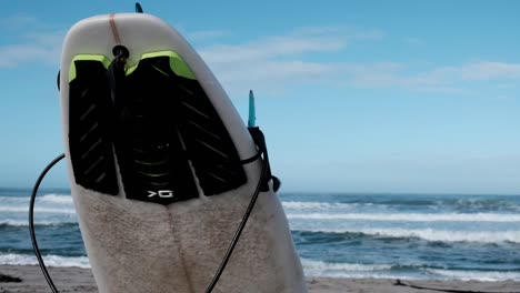 Surfboard-with-deck-pad,-fins-and-a-leash-at-the-beach