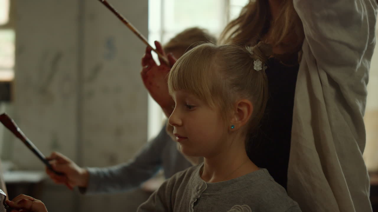 쾌활한 여성 선생님이 실내에서 걸작을 만들고 있습니다.  ⁇ 솔 stroke를 만드는 소녀.