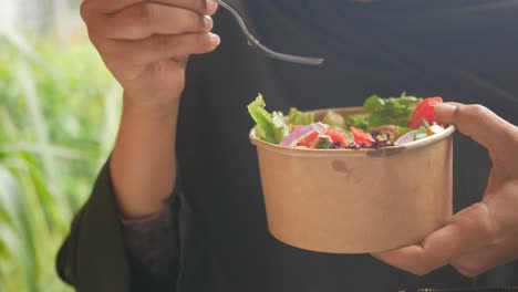 person eating a fresh salad from a disposable bowl