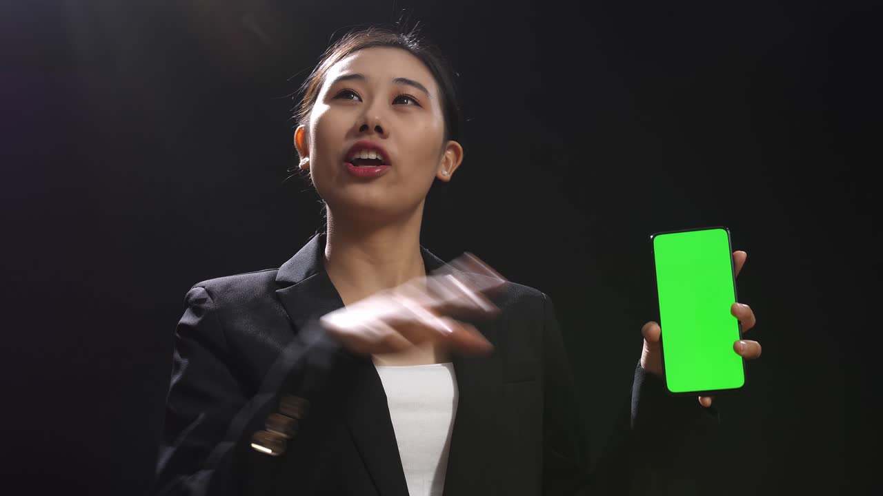 블랙 스크린 스튜디오에서 말하는 동안 녹색 스크린 스마트폰을 들고 있는 비즈니스 슈트를 입은 아시아 스피커 여성의 클로즈업