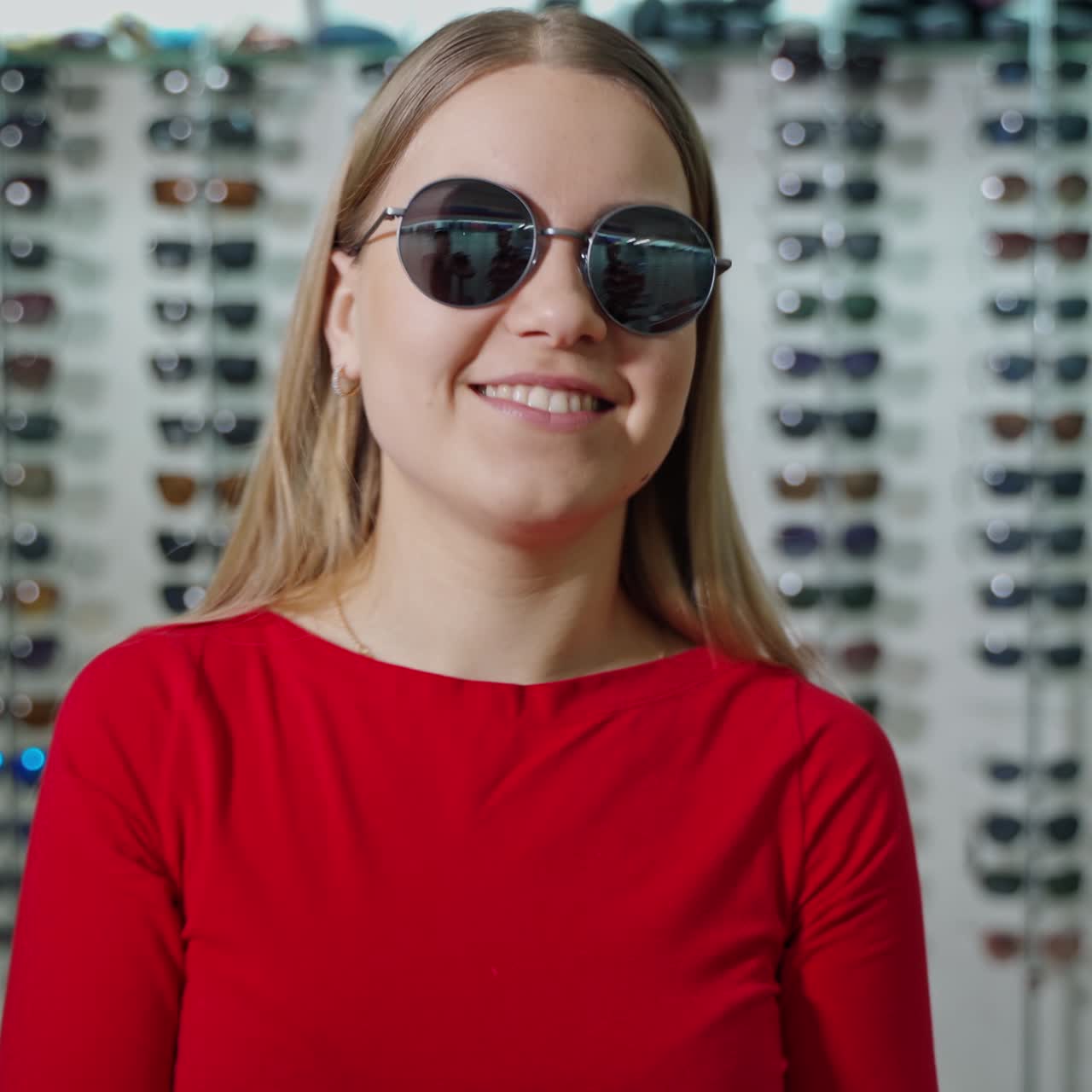 Portrait of attractive girl choosing sunglasses. Female buyer is posing on camera in new trendy glasses in the optics store.