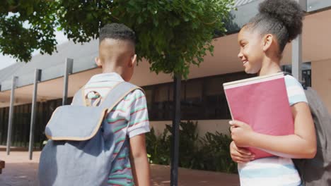 video of three happy diverse schoolchildren with schoolbags talking, walking into school