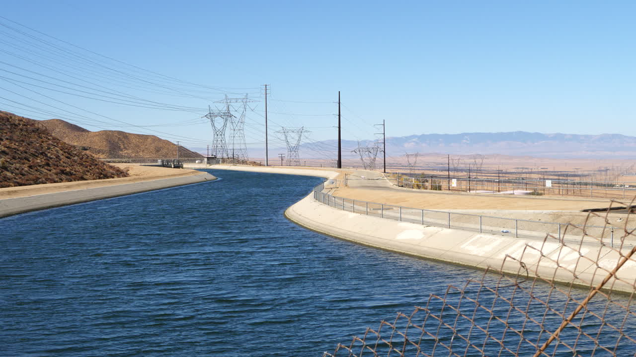 가뭄 동안 로스 앤젤레스로 향하는 푸른 물 공급으로 가득 찬 캘리포니아 수로의 체인 링크 울타리를 통해 슬라이딩 샷