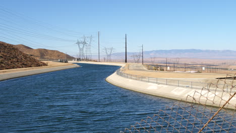 Sliding-shot-through-a-chain-link-fence-of-the-California-Aqueduct-full-of-blue-water-supply-heading-into-Los-Angeles-during-a-drought