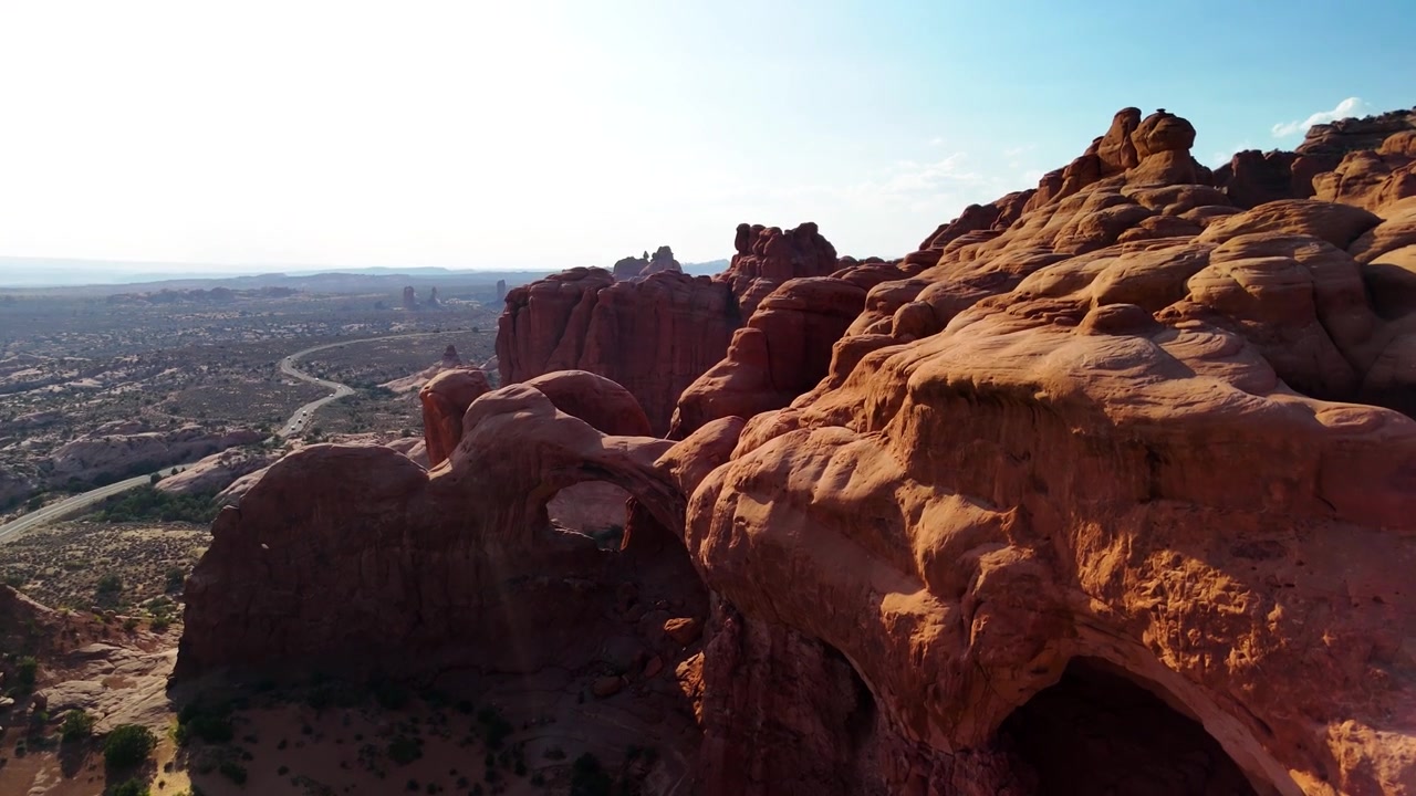 Splendido filmato stock del Parco Nazionale di Arches, USA, durante un pomeriggio luminoso. La luce solare brillante illumina le maestose strutture di arenaria rossa e il paesaggio desertico sotto un cielo azzurro limpido.