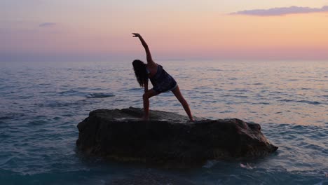 una atleta posa ejercicios de yoga sobre un acantilado rodeado de agua de mar al atardecer con un cielo brillante