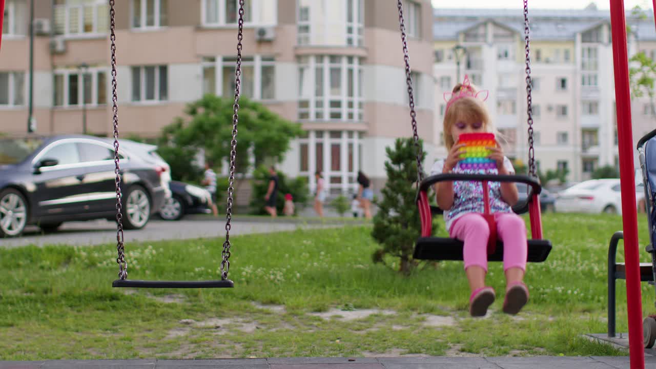 Bambino/a alla moda gioca con il popolare giocattolo sensoriale Pop It a bolle morbide sull'altalena del parco giochi