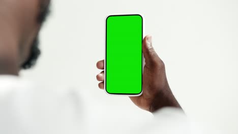 young person use smartphone with green screen chroma key close-up. guy look hold in hand cell phone mock-up. concept watch and show internet social media, video calls, read news, app, iot, e-shopping