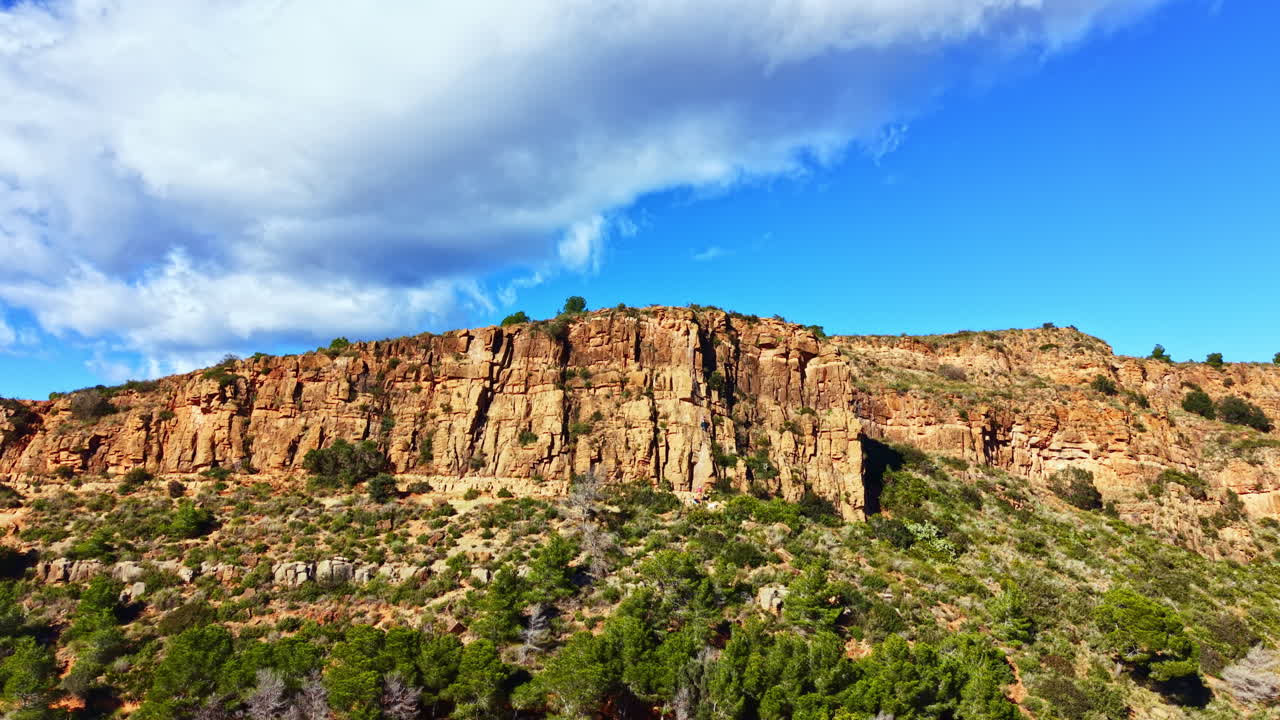 Formazioni rocciose e alberi verdi sotto un cielo blu vicino a un canyon di giorno in una zona rurale.