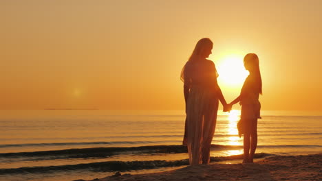 Mama-Und-Tochter-Freuen-Sich-Auf-Einen-Wunderschönen-Sonnenuntergang-über-Dem-Meer-Silhouetten-Einer-Frau-Mit