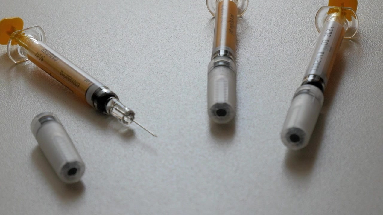 白い台の上に置かれた3本の注射器を映し出す右パンショット。1本は開いており、他はキャップがされている。