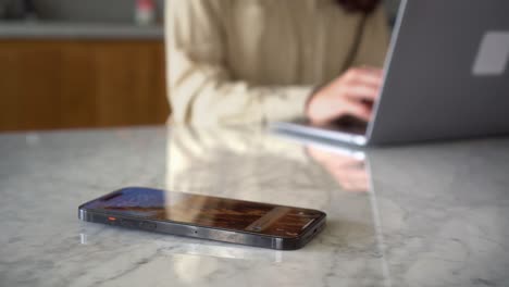 mujer trabajando en segundo plano y pierde el texto de notificación telefónica en su teléfono inteligente mientras se concentra en su trabajo