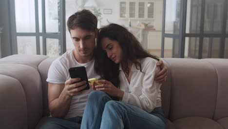 happy couple sitting on sofa with mobile phones together.