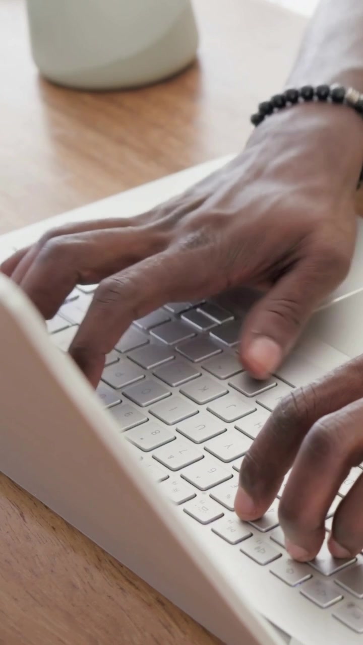 Verticale video: Typende handen van een man werkend op een witte laptop op een houten bureau, pauzerend, telefoon inspecterend