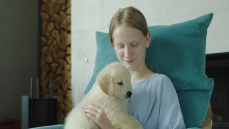 A-teenage-girl-plays-with-a-puppy-of-a-golden-retriever,-sits-in-an-armchair-near-the-fireplace