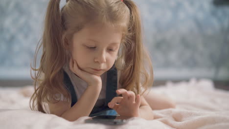 sad girl plays with mobile phone lying on floor with blanket