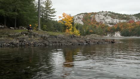 Man-Camps-on-Shore-of-Calm-Lake-in-Autumn-Forest-Colors,-Wide-Tilt-Up