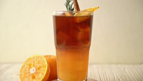 a glass of iced americano black coffee and layer of orange and lemon juice decorated with rosemary and cinnamon