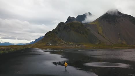 un fotógrafo con una chaqueta amarilla caminando en la playa de hofn