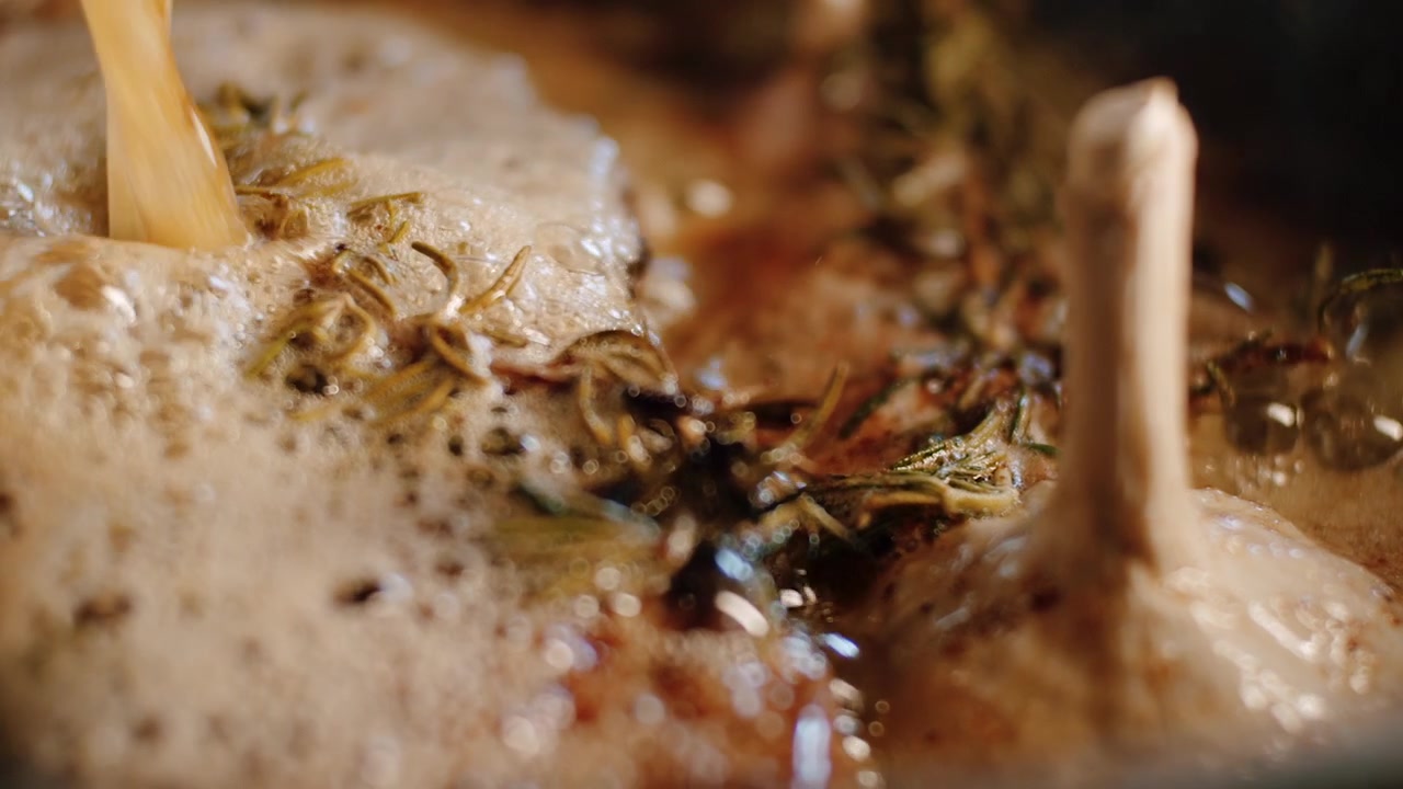 Meat in pan basting technique with sizzling froth of butter, garlic bulb and rosemary as flavor