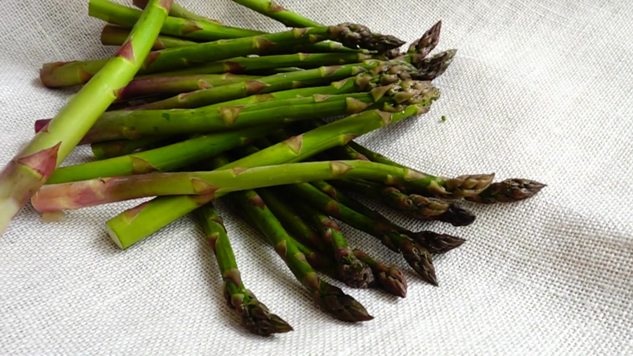 Verse groene asperges vallen op jute. Slowmotion.