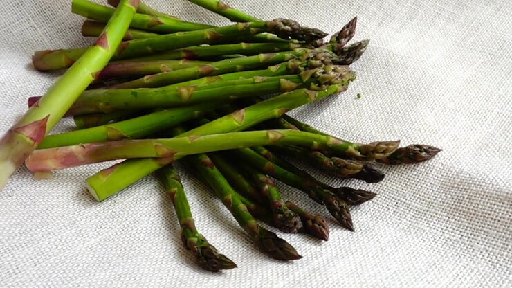 Fresh green asparagus falls on burlap. Slow motion.