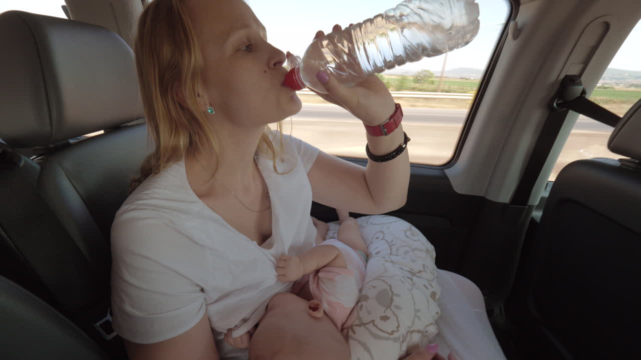 madre amamantando al bebé y bebiendo agua en un coche en movimiento
